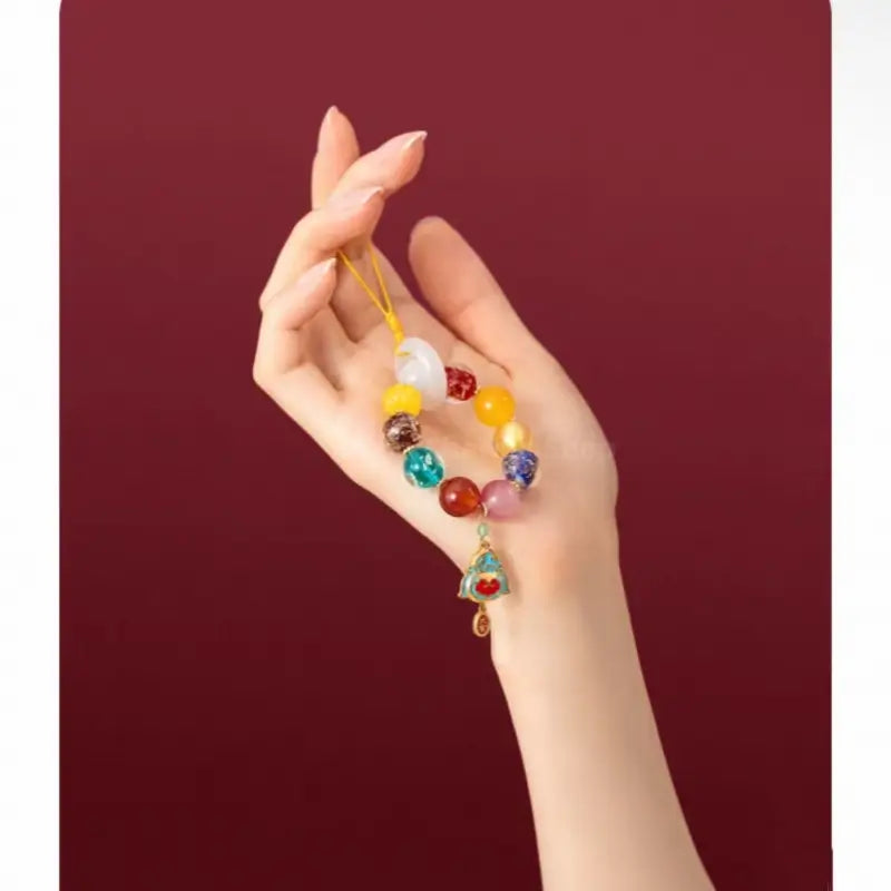 Hand displaying colorful gemstone beaded phone charm bracelet with enamel lock pendant.