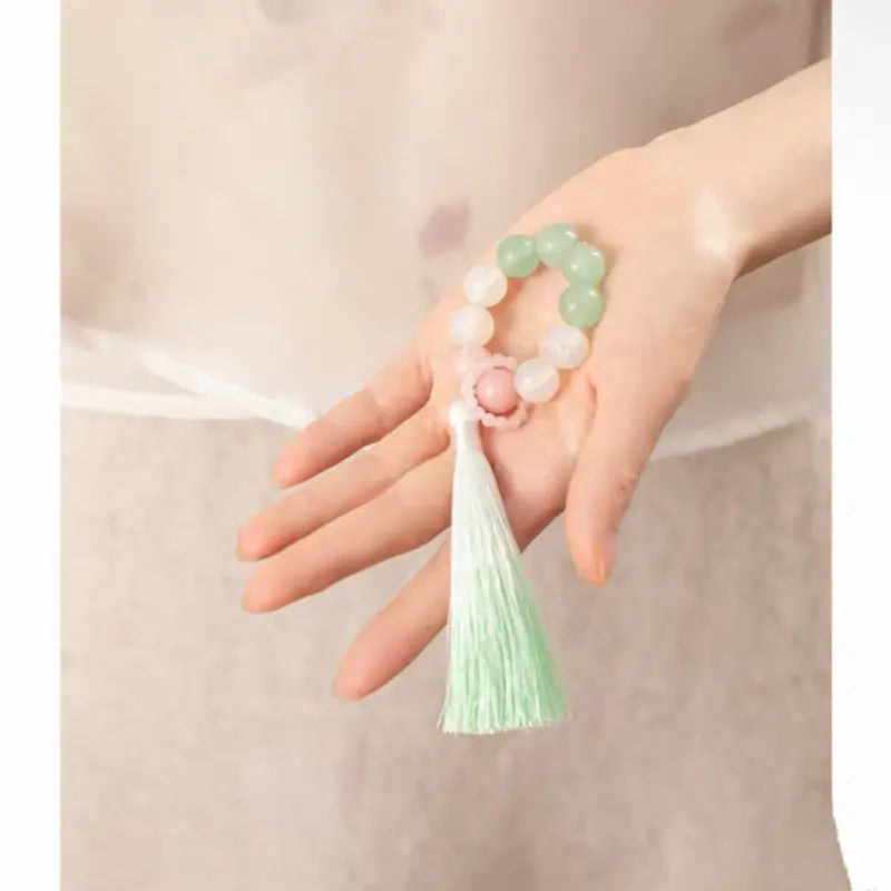 Hand holding soft green jadeite and quartz beaded phone strap with long silk tassel.