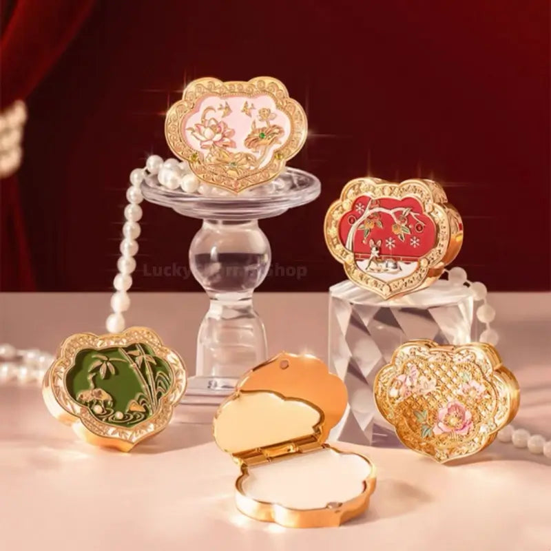 Five ornamental gold Palace Museum Ruyi solid perfume compacts in pink, red, green, and gold styles with pearls.