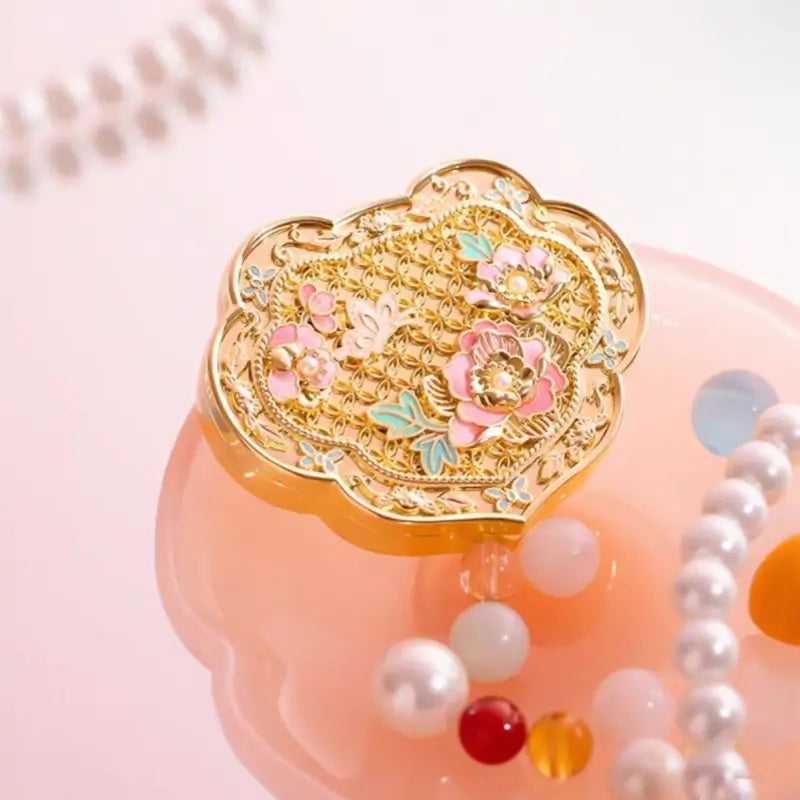 Gold filigree Ruyi solid perfume compact with enamel peony flowers displayed on pink lotus dish with pearls.