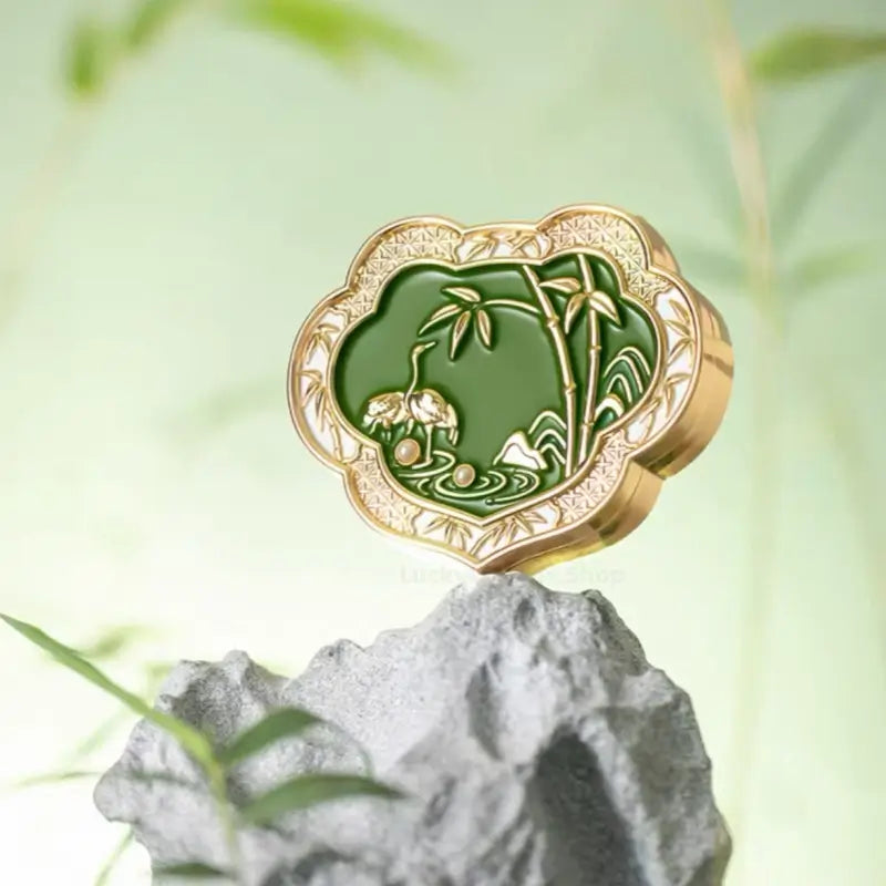 Palace Museum green enamel Ruyi solid perfume compact with crane and bamboo design placed on miniature rockery.