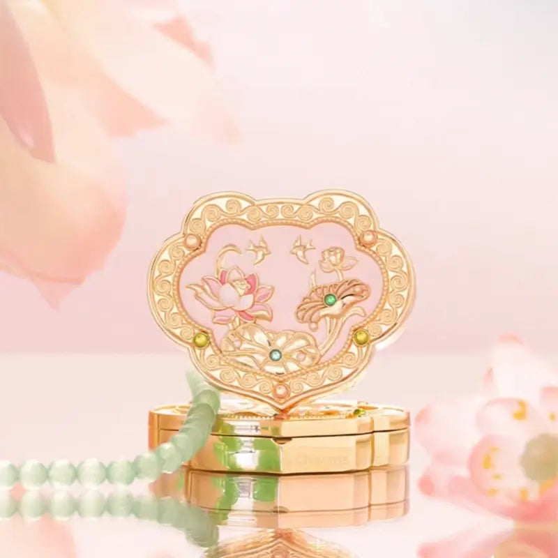 Pink enamel lotus Ruyi solid perfume compact with gold swallows displayed with jade bead strand and flowers.