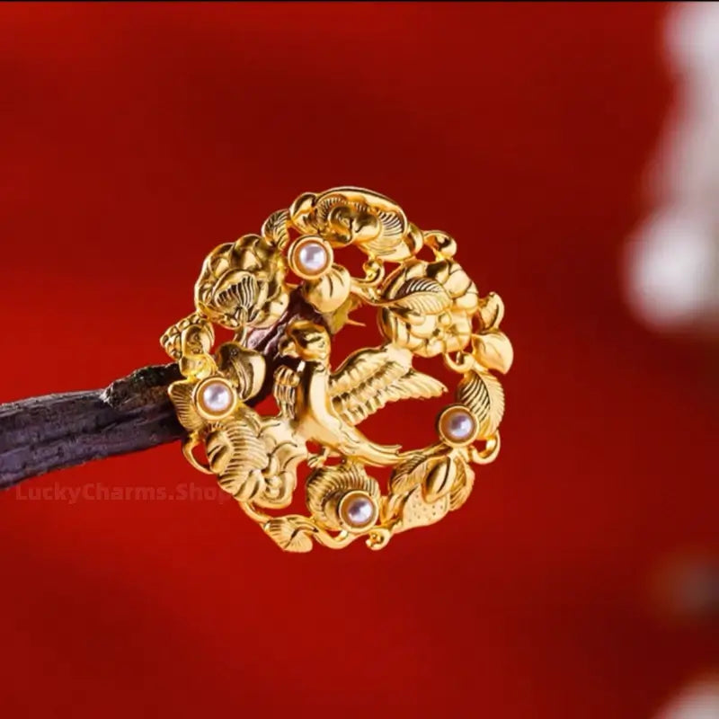 Gold-plated bird and pearl medallion brooch mounted on wooden branch display.