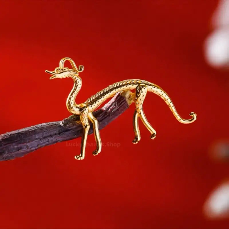 Gold-plated Chinese dragon brooch displayed on wooden branch against red backdrop.
