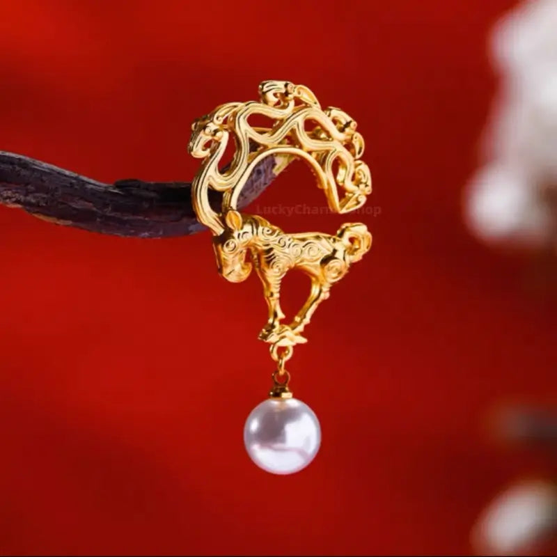 Gold-plated auspicious deer brooch with dangling pearl bead on wooden display branch.