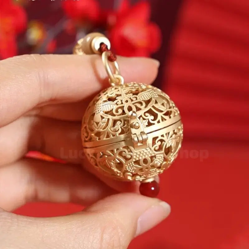 Hand holding a gilded silver hollow spherical sachet pendant with delicate traditional bird and flora engravings.