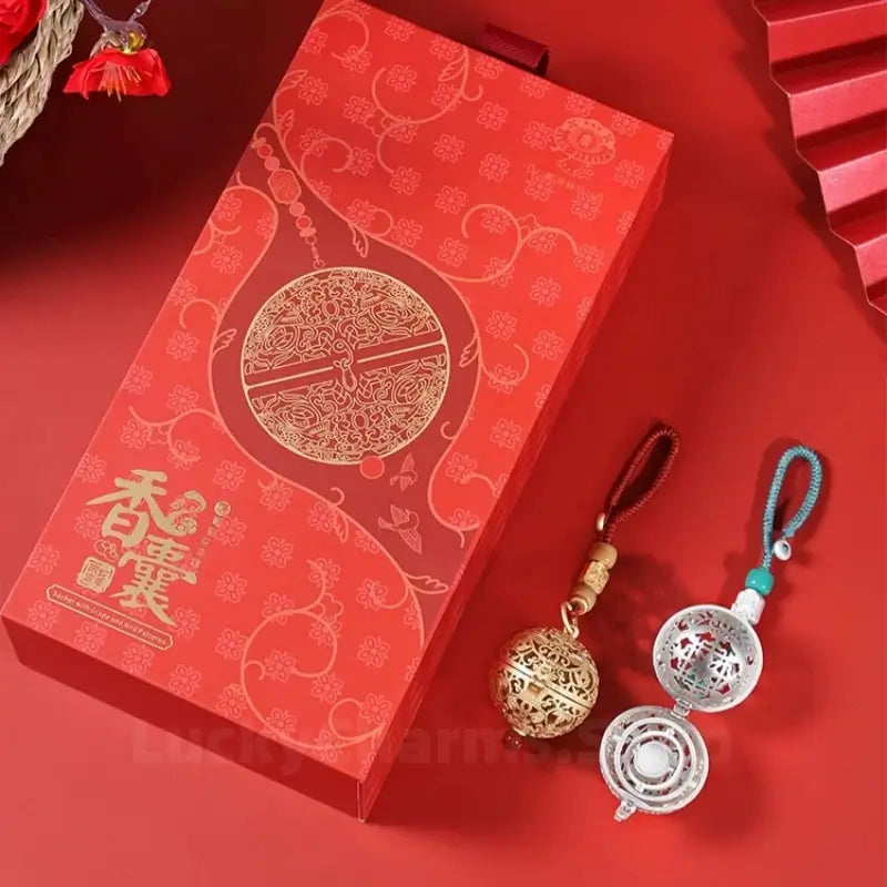 Chinese-style gold and silver spherical sachet pendants next to a red presentation gift box.