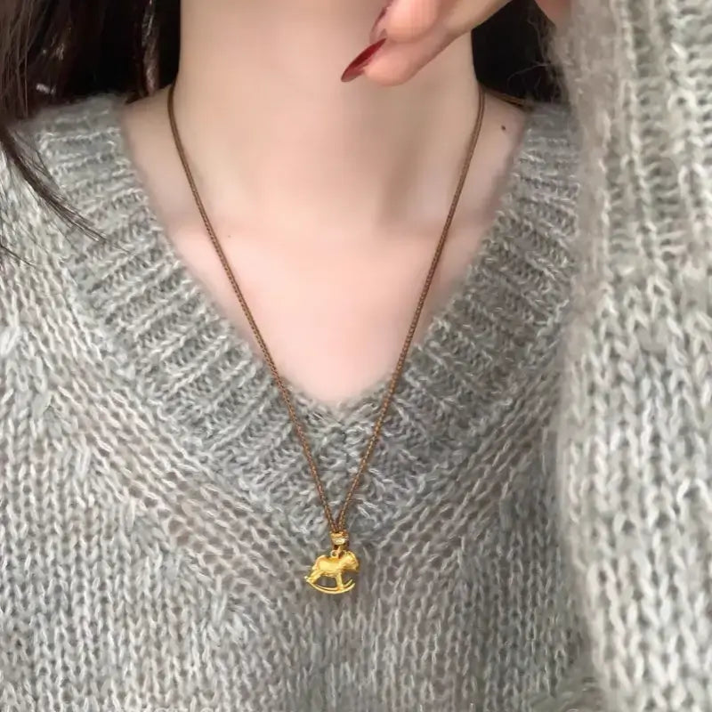Model wearing gold carousel horse pendant sweater chain over grey knitted sweater.