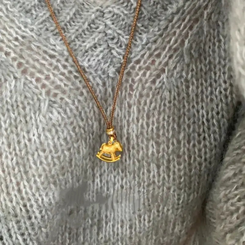 Close-up of gold rocking horse pendant necklace worn on a grey sweater.