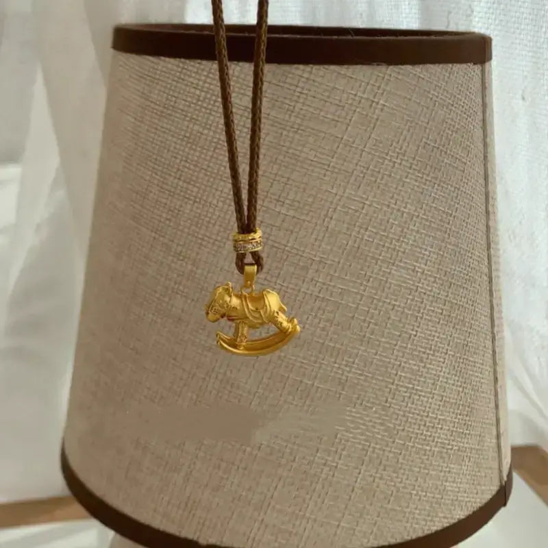 Gold-plated carousel horse charm sweater necklace displayed against fabric lampshade.