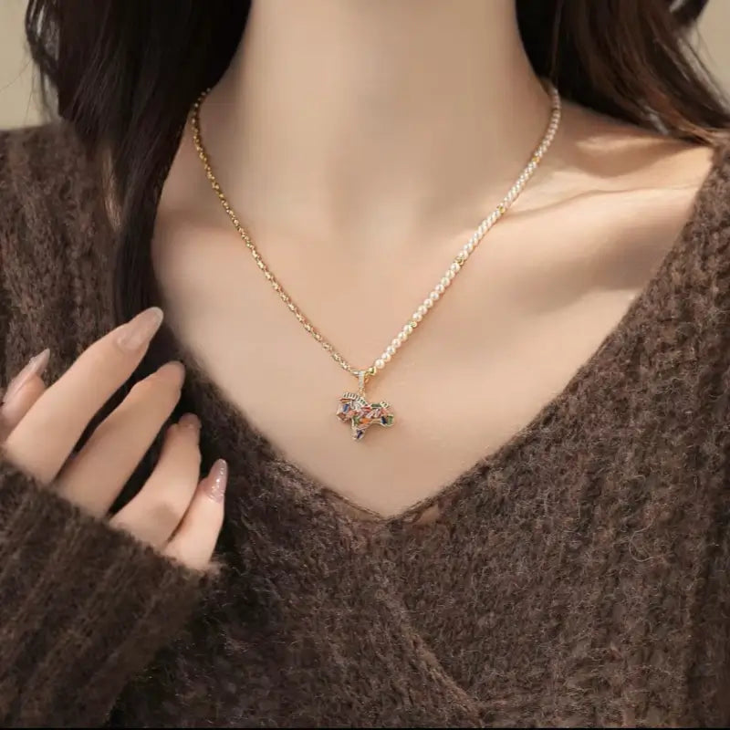 Model wearing gold and pearl chain necklace with colorful zircon horse pendant.