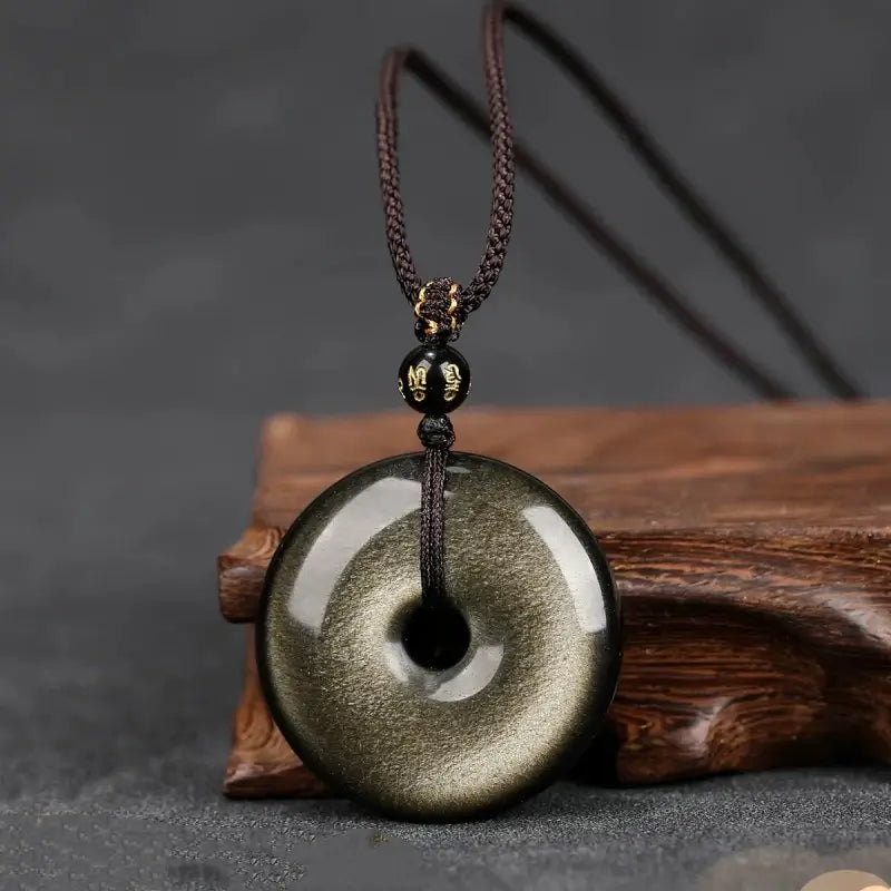 Gold sheen obsidian peace buckle donut pendant necklace displayed on a wooden block stand.