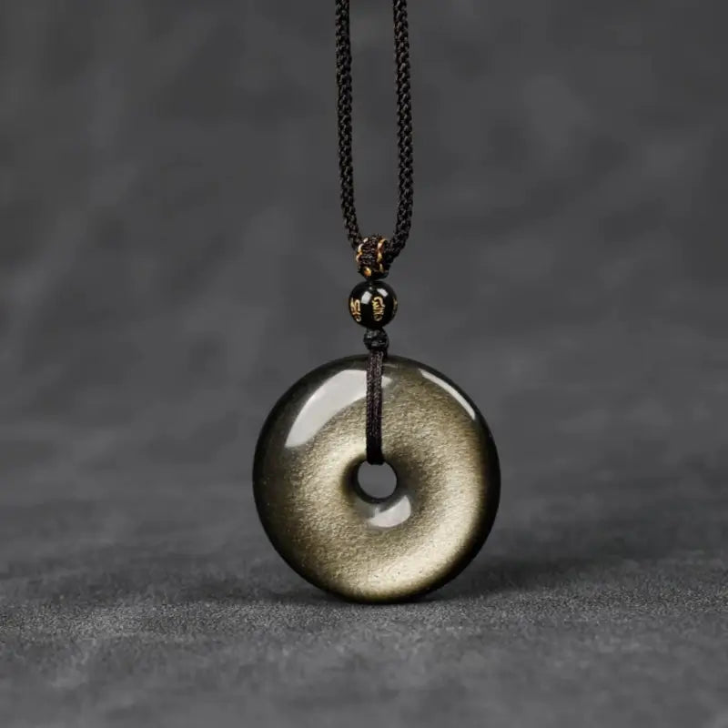 Front view of natural gold sheen obsidian Ping An Kou protection pendant on adjustable black cord.