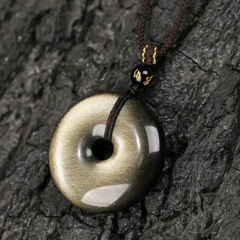 Close-up of glossy natural gold sheen obsidian peace buckle donut pendant on dark wood texture.