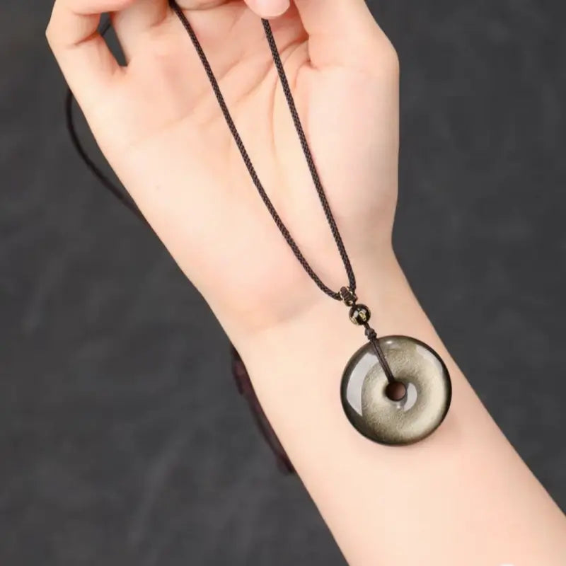 Model wearing natural gold sheen obsidian peace buckle donut lucky amulet pendant on wrist.