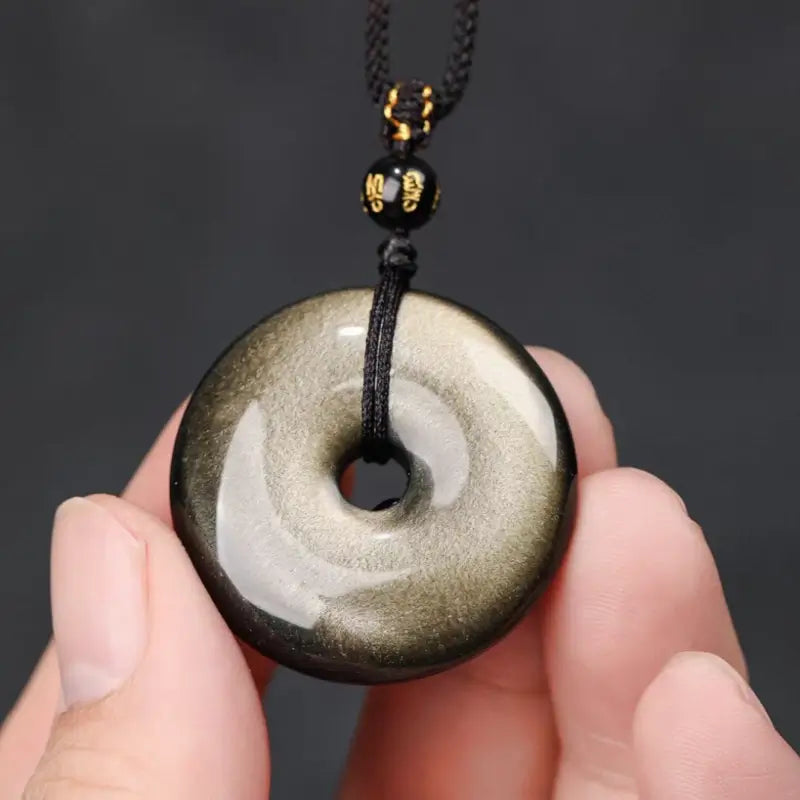 Hand holding polished gold sheen obsidian Ping An Kou protection pendant showing natural sheen.