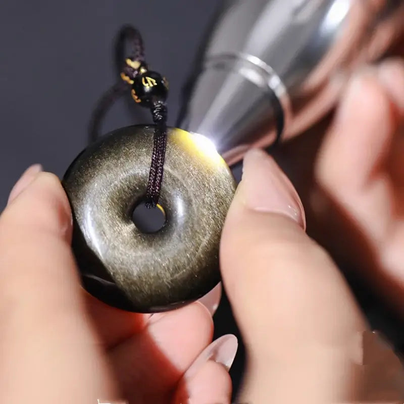 Flashlight test revealing authentic sheen and translucency of gold obsidian peace buckle pendant.