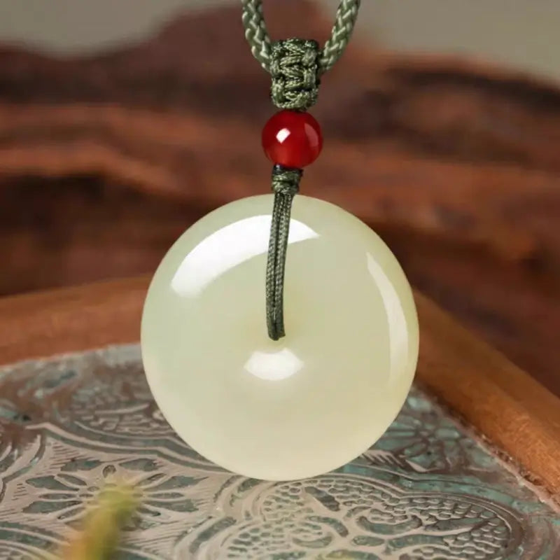 Smooth Hetian nephrite jade donut charm necklace with red agate accent bead and cord.