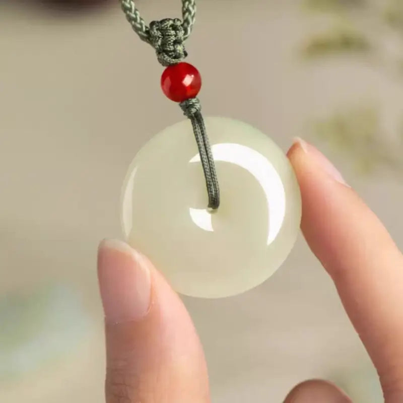 Person holding a translucent natural Hetian jade peace buckle protection amulet pendant.