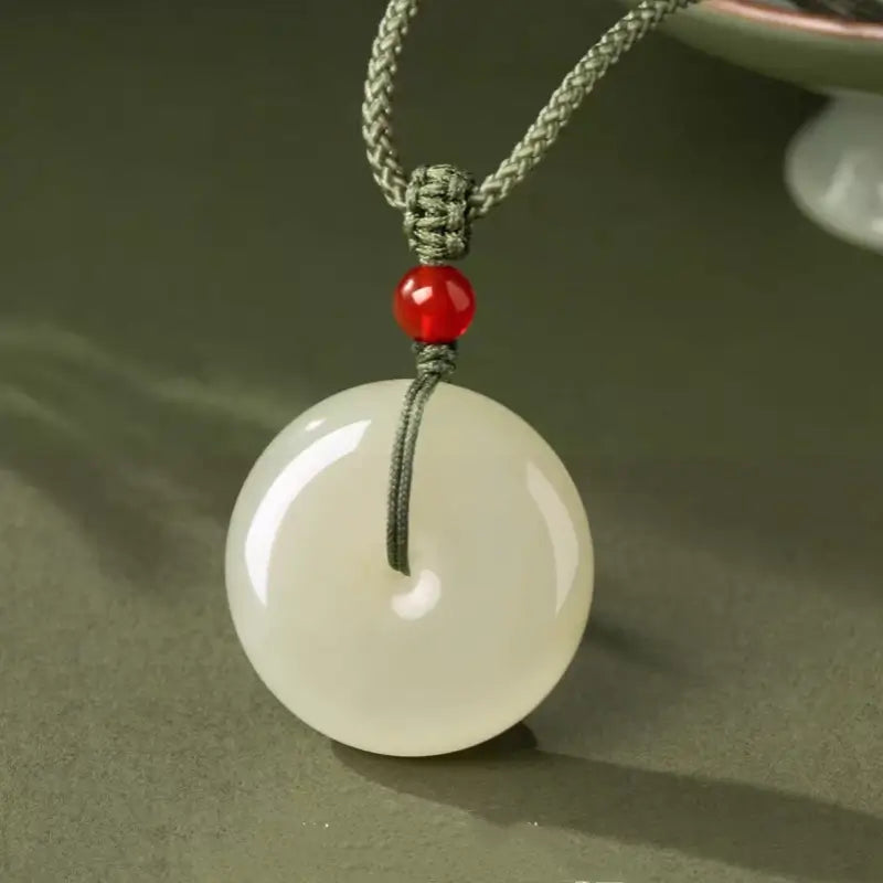 Chinese natural Hetian jade protection disc pendant on braided green cord necklace.