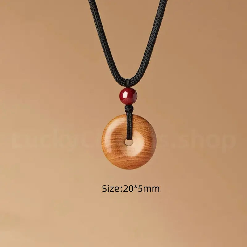 Small size peach wood donut pendant necklace with black cord measuring 20 by 5 millimeter.