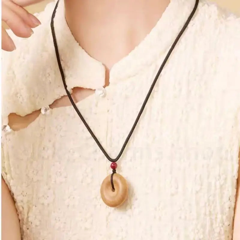 Woman wearing natural peach wood peace buckle pendant necklace on cream dress.