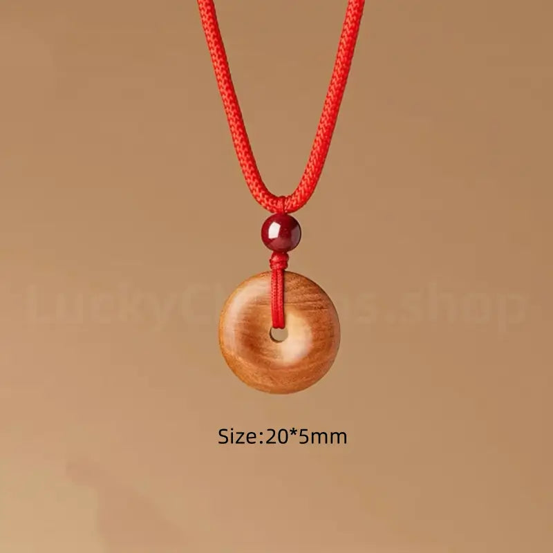Small peach wood donut pendant necklace on adjustable red string measuring 20 by 5 millimeter.