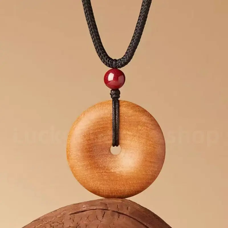 Natural peach wood peace buckle pendant necklace with cinnabar bead on black cord.