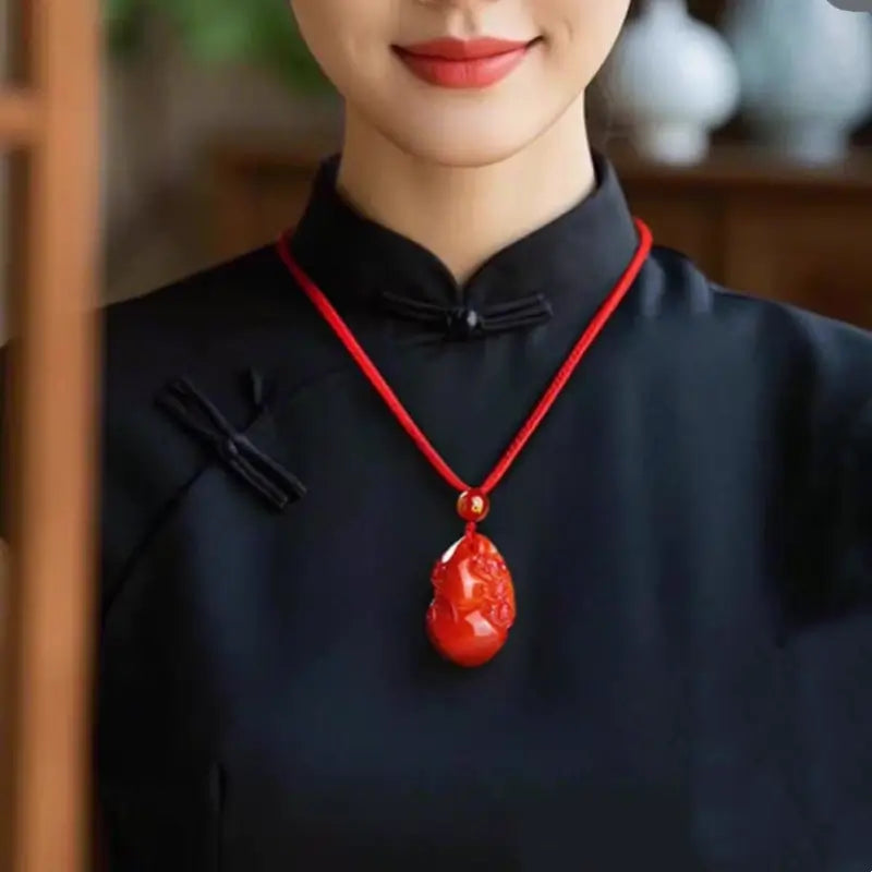 Woman wearing carved red agate Pixiu gourd pendant necklace over dark outfit.