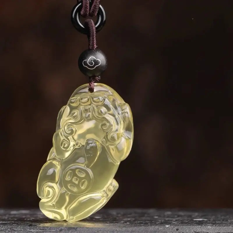 Carved translucent natural citrine Pixiu pendant with a coin motif on a dark braided cord.