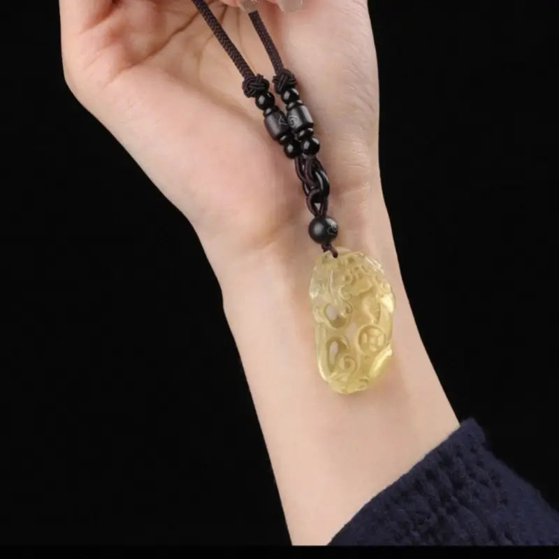 Person holding a yellow natural citrine Pixiu wealth pendant with black accent beads.