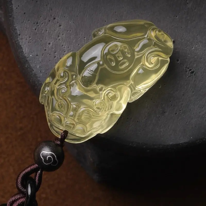 Close-up of yellow citrine quartz Pixiu carving featuring an ancient coin detail on dark slate.