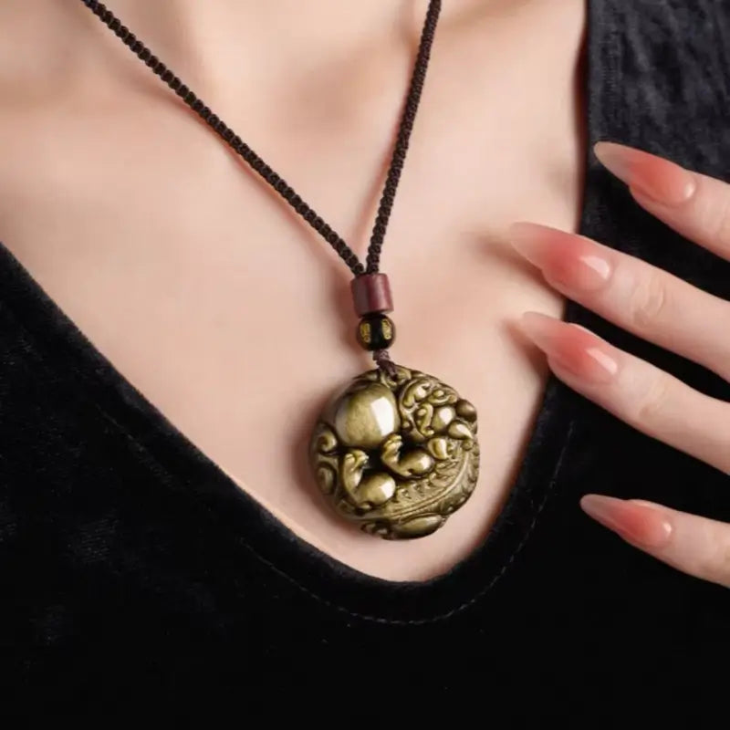 Person wearing a round gold sheen obsidian Pixiu necklace over a black velvet top.