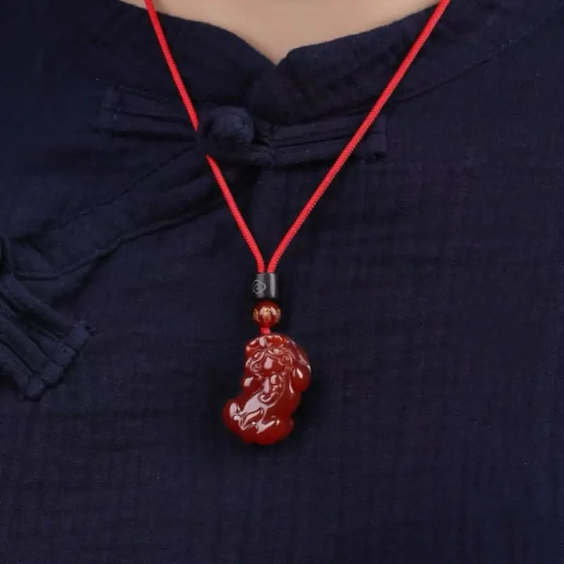 Person wearing a natural red agate Pixiu pendant necklace with red adjustable cord.