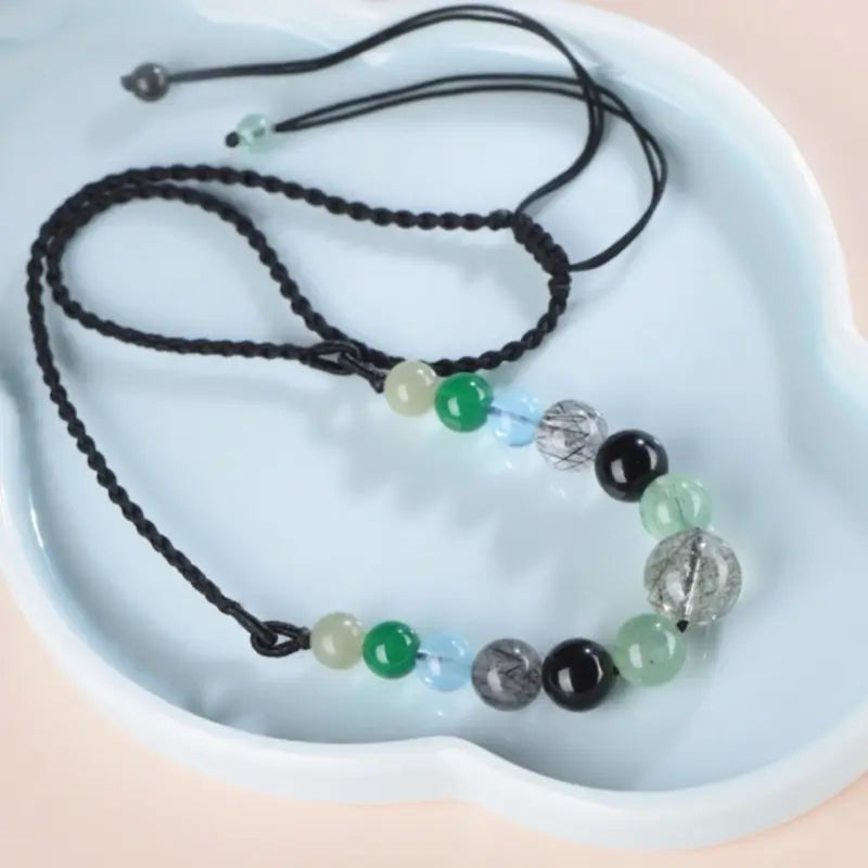 Five Elements beaded natural crystal necklace displayed on a light blue decorative ceramic plate.
