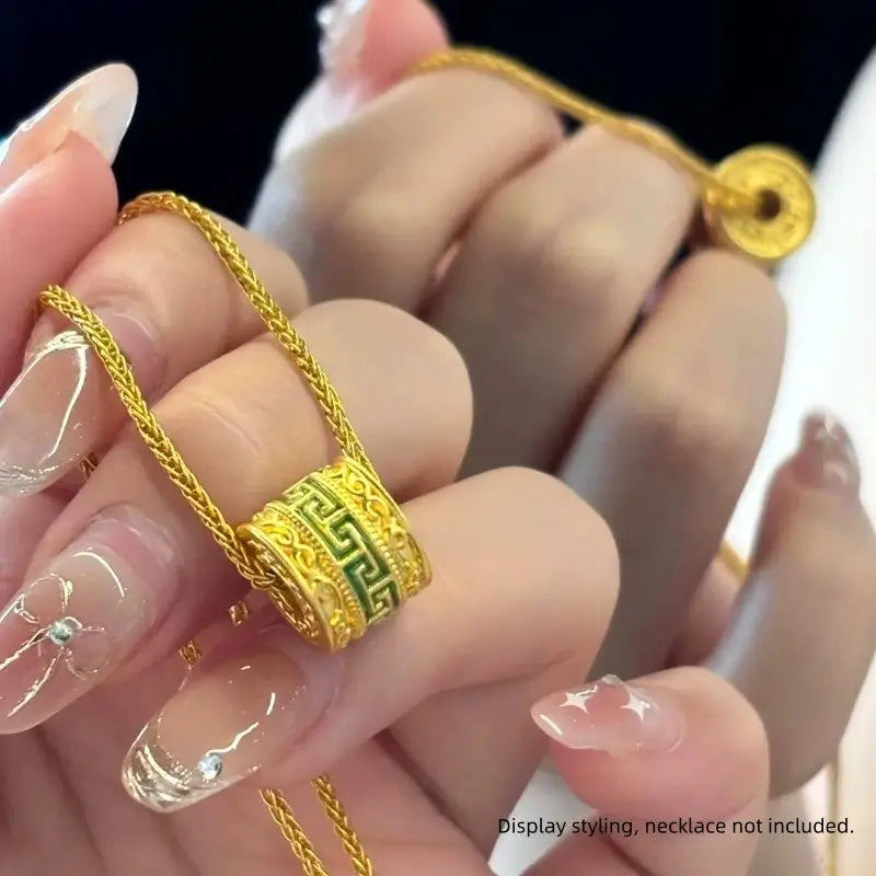Hand holding gold chain featuring green enamel and gold meander pattern Lu Lu Tong charm bead.