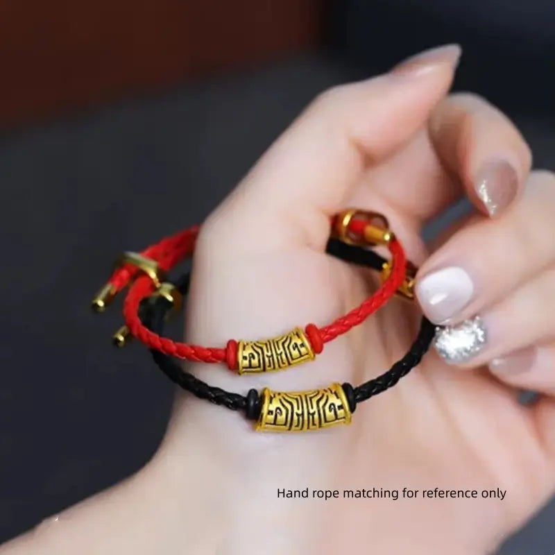 Hand holding red and black braided cord charm bracelets with gold-plated Chinese Taotie pattern beads.