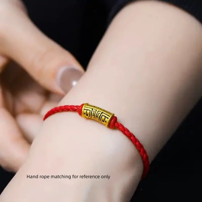 Close-up of a red braided cord bracelet featuring a gold-plated Chinese Taotie pattern Lu Lu Tong bead on a wrist.