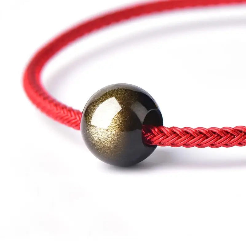 Polished gold sheen obsidian large hole spacer bead on braided red cord.
