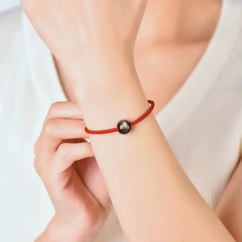 Woman wearing a red cord bracelet featuring a gold sheen obsidian bead.