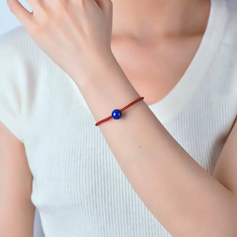 Woman wearing a woven red string bracelet with a blue lapis lazuli bead.