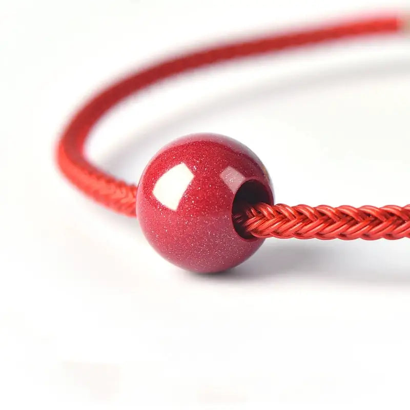 Close-up of a sparkling red purple gold sand cinnabar bead threaded on a matching red cord.