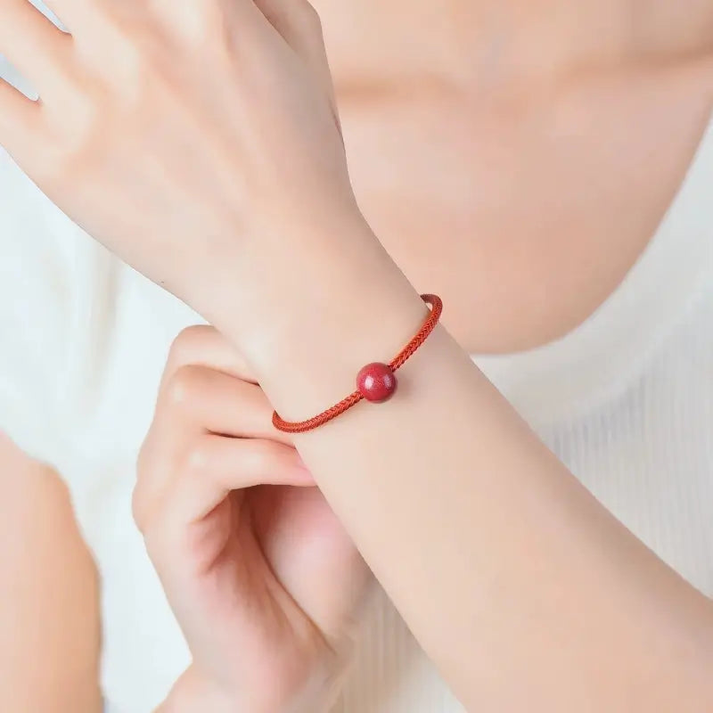 Woman wearing a minimal red string bracelet featuring a single purple gold sand cinnabar bead.