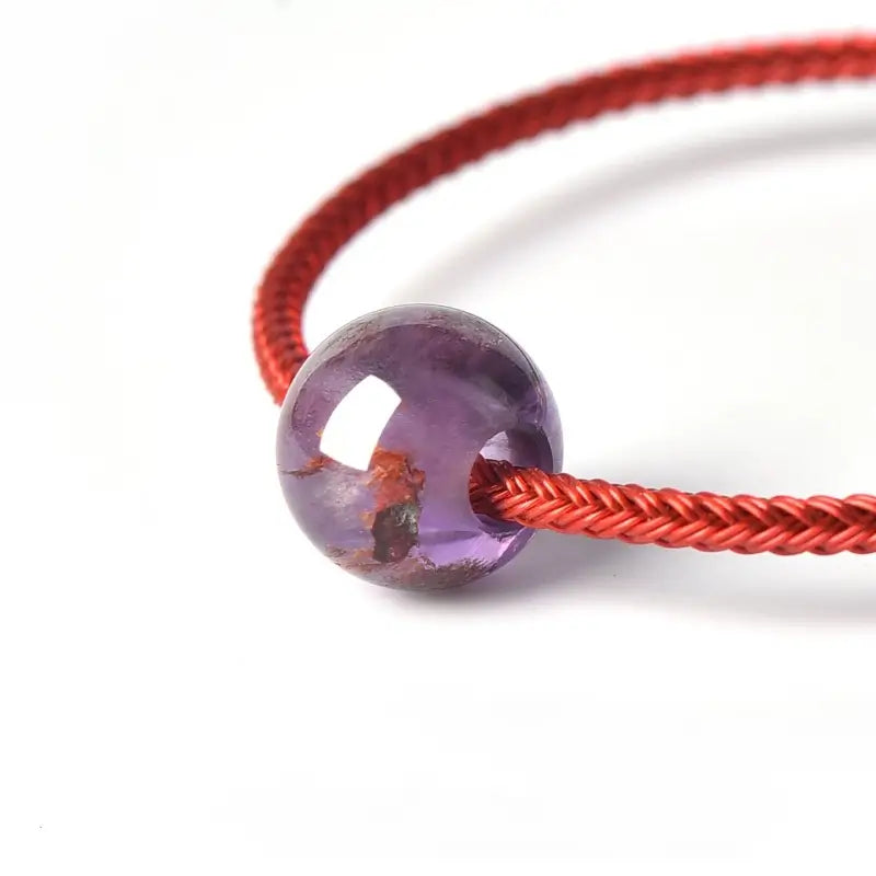 Close-up of natural purple phantom quartz bead threaded onto a red braided jewelry cord.