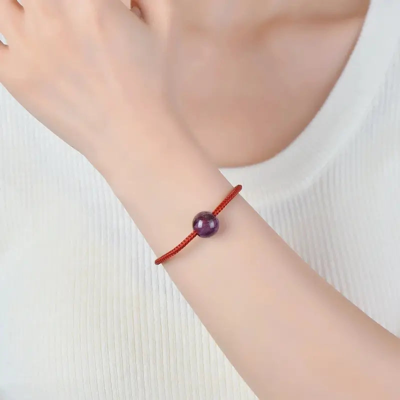 Woman wearing a minimal red string wrist bracelet featuring a purple phantom quartz bead.
