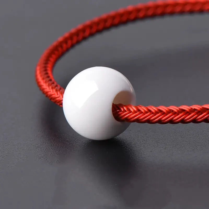 Close-up of smooth white shell bead threaded onto a red braided cord.
