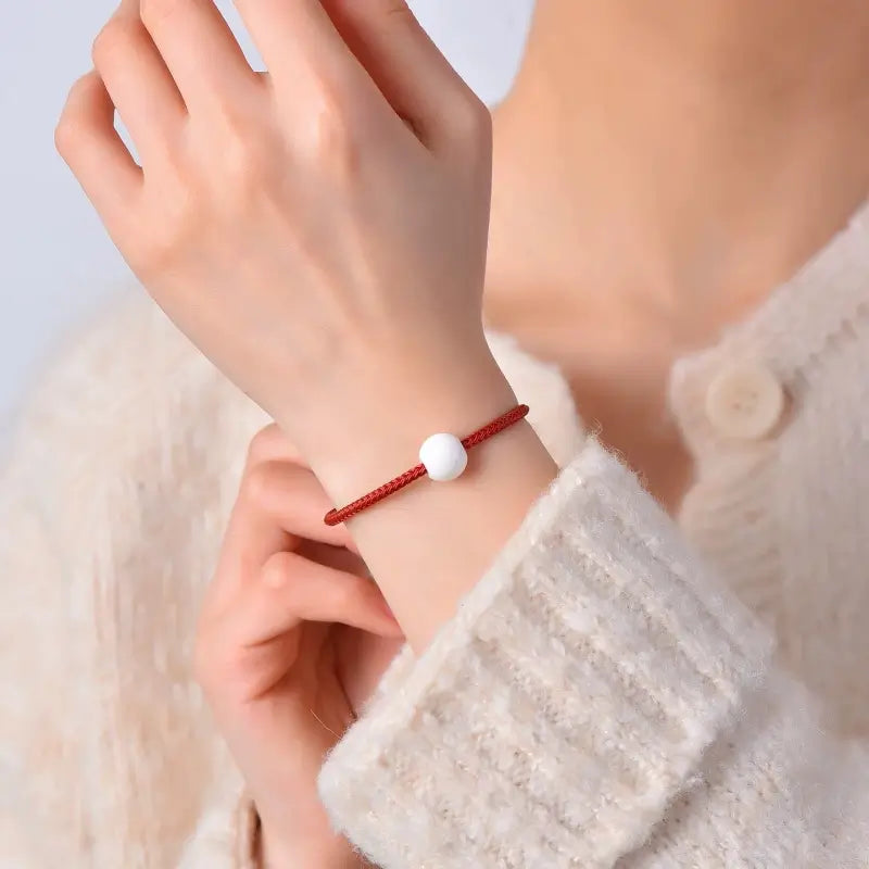 Woman wearing a thin red string wrist bracelet set with a smooth white shell bead.
