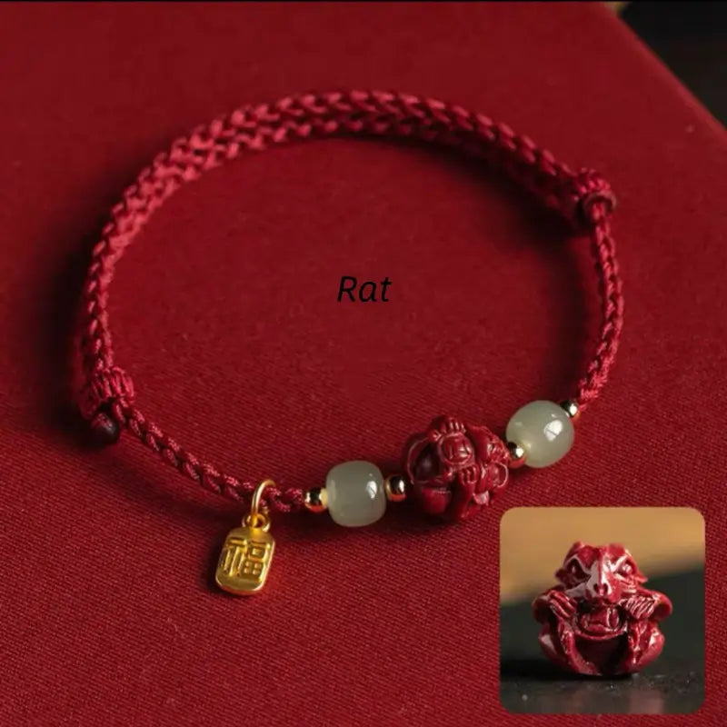 Hand-woven red cord bracelet featuring carved Rat zodiac cinnabar bead and gold Fu blessing tag.