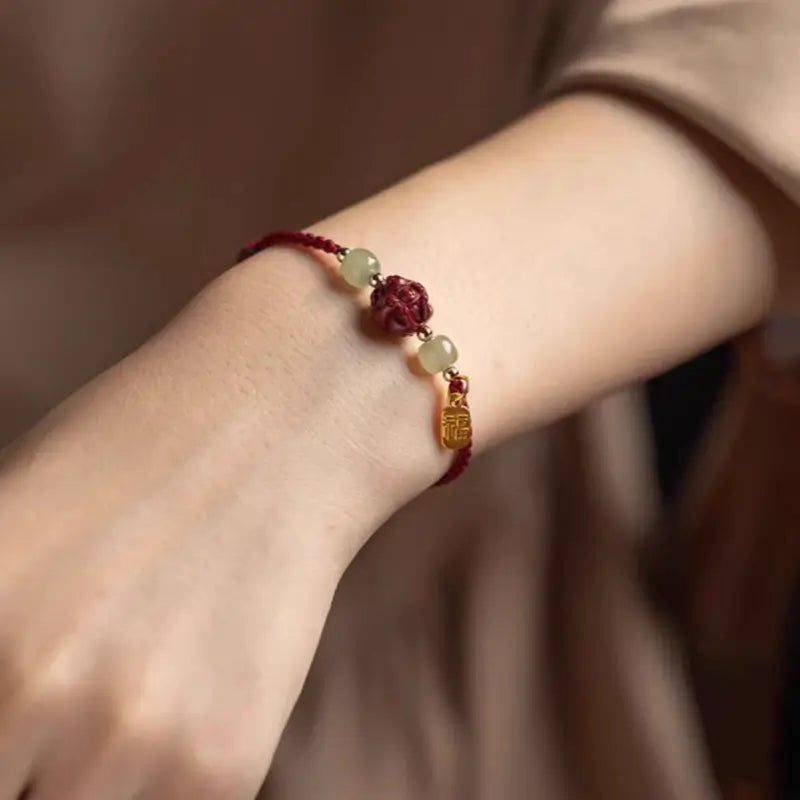 Model wearing red braided string fortune bracelet with carved cinnabar zodiac charm and Hetian jade beads.
