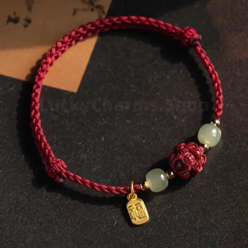 Top-down view of hand-woven red cord bracelet featuring carved red cinnabar zodiac bead and gold pendant.